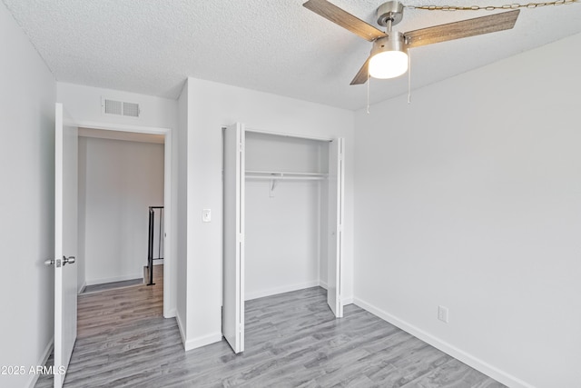 unfurnished bedroom featuring ceiling fan, a closet, light hardwood / wood-style floors, and a textured ceiling