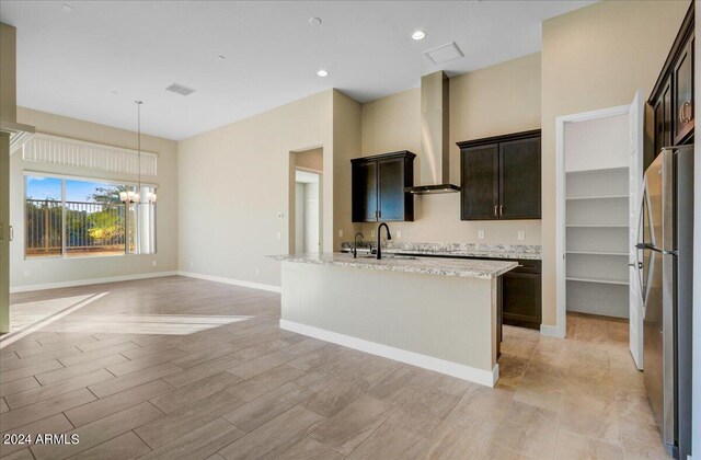 kitchen with light stone counters, stainless steel fridge, a center island with sink, light hardwood / wood-style flooring, and an inviting chandelier