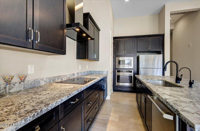 kitchen featuring light stone counters, dark brown cabinetry, sink, wall chimney range hood, and appliances with stainless steel finishes