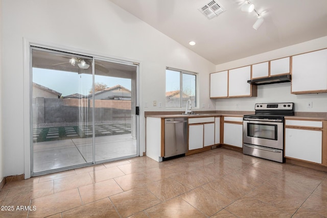 kitchen featuring sink, rail lighting, white cabinetry, stainless steel appliances, and vaulted ceiling