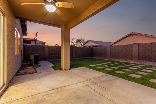 patio terrace at dusk featuring ceiling fan and a yard