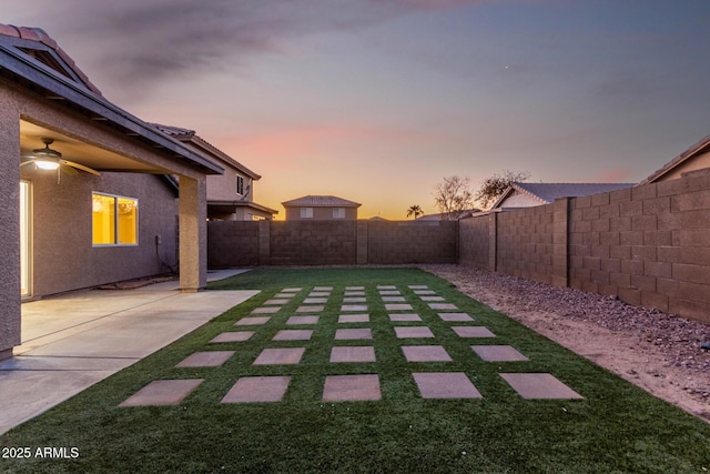 yard at dusk with ceiling fan and a patio area