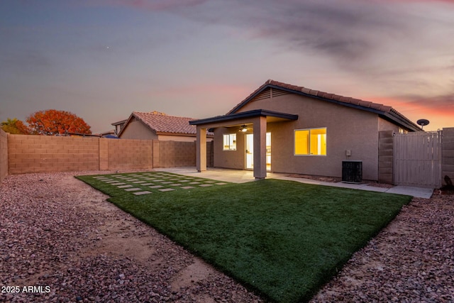 back house at dusk featuring cooling unit, ceiling fan, a patio, and a lawn