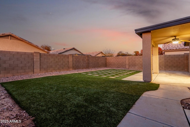 yard at dusk featuring a patio and ceiling fan