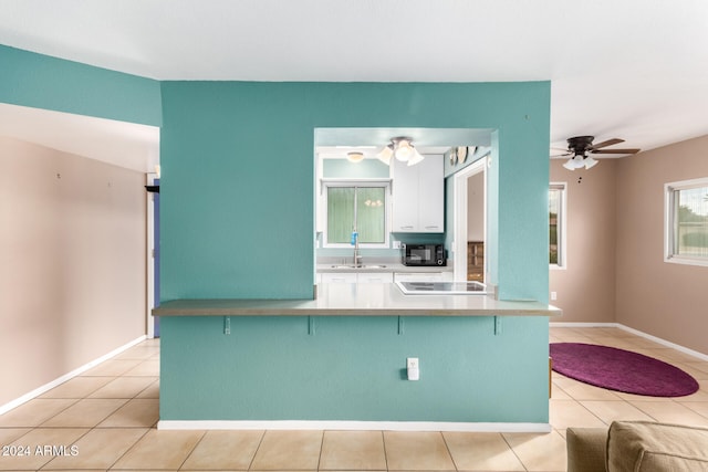 kitchen with sink, ceiling fan, light tile patterned floors, kitchen peninsula, and a breakfast bar area