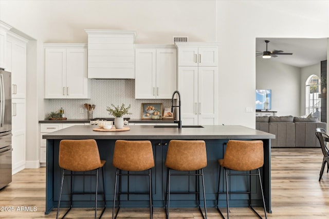 kitchen with light wood-type flooring, sink, a center island with sink, and white cabinets