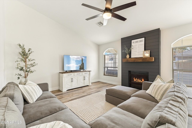 living room featuring lofted ceiling, a large fireplace, ceiling fan, and light wood-type flooring