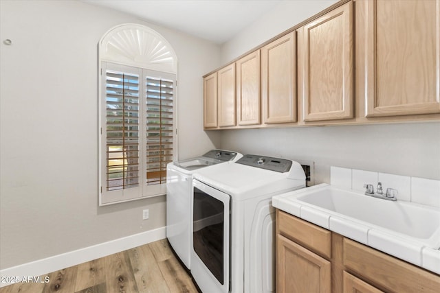 laundry area featuring light hardwood / wood-style floors, sink, washing machine and dryer, and cabinets