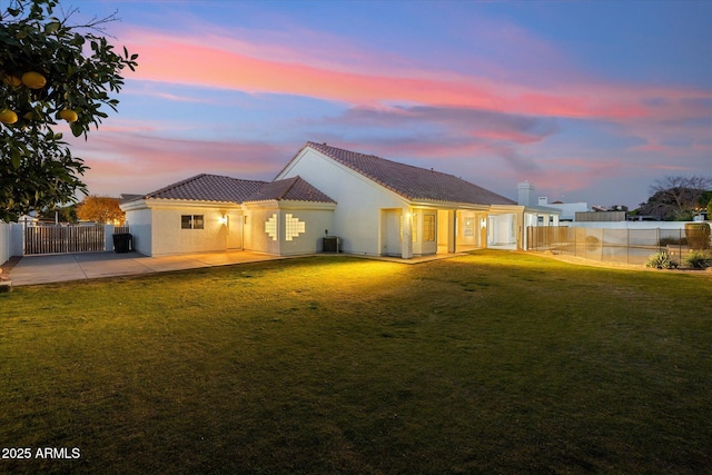 back house at dusk featuring cooling unit, a yard, and a patio