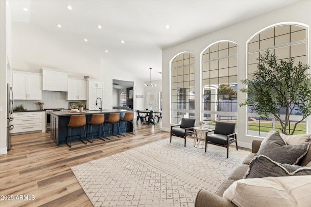 living room with an inviting chandelier, a towering ceiling, sink, and light hardwood / wood-style floors