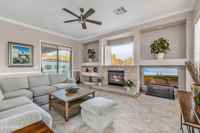 living room featuring ceiling fan, crown molding, built in features, and a tiled fireplace