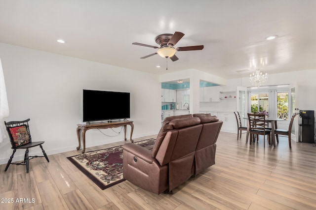 living room with ceiling fan with notable chandelier, light hardwood / wood-style floors, and sink