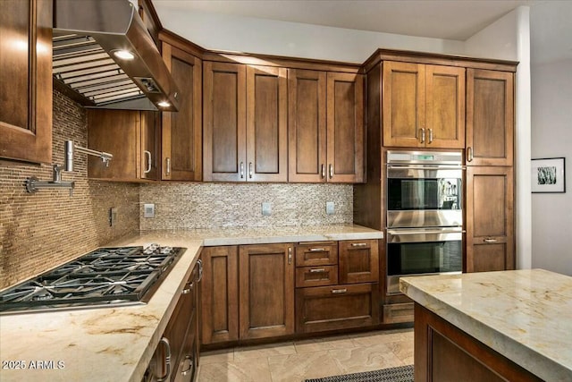 kitchen with appliances with stainless steel finishes, backsplash, wall chimney range hood, and light stone counters