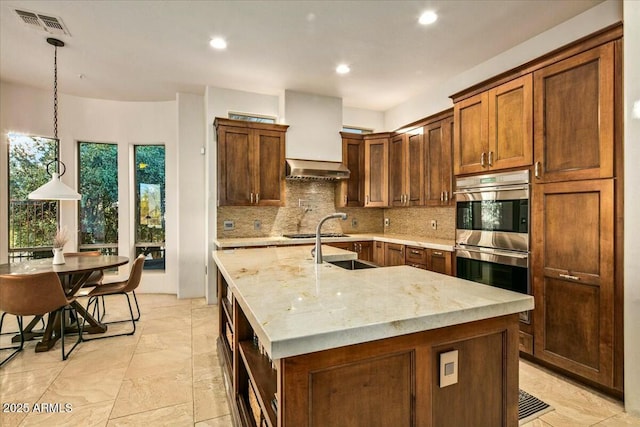 kitchen with stainless steel appliances, exhaust hood, visible vents, backsplash, and a center island with sink