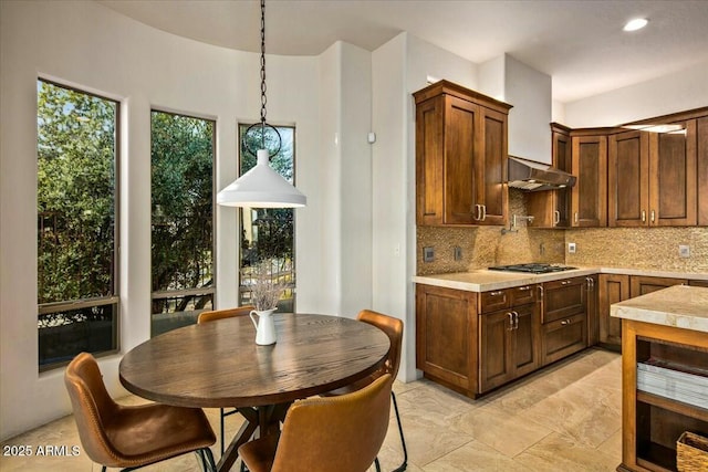 kitchen featuring light countertops, stainless steel gas stovetop, hanging light fixtures, decorative backsplash, and under cabinet range hood