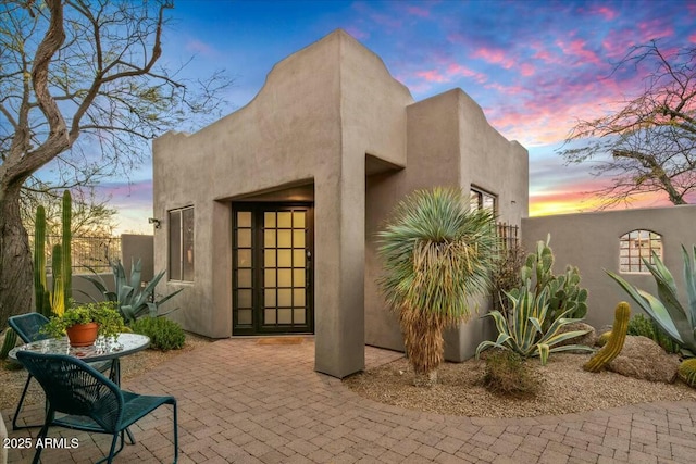 exterior entry at dusk with a patio, fence, and stucco siding