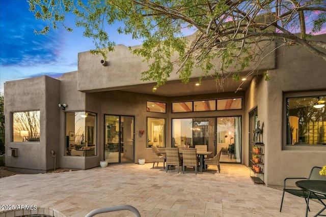 rear view of house with outdoor dining space, a patio area, and stucco siding