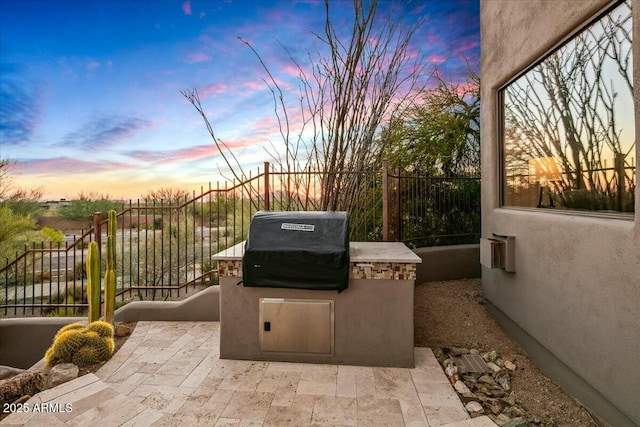 patio terrace at dusk featuring exterior kitchen, grilling area, and fence