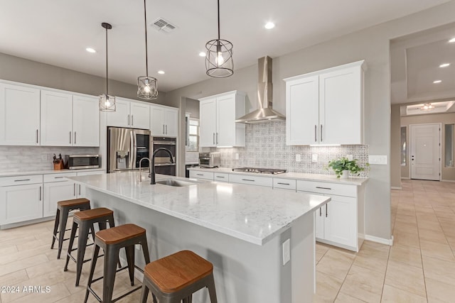 kitchen featuring hanging light fixtures, white cabinets, stainless steel appliances, and wall chimney range hood