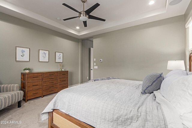 bedroom featuring ceiling fan, light colored carpet, and a tray ceiling