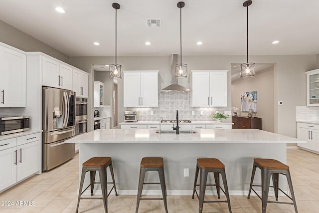 kitchen with a breakfast bar, a center island with sink, wall chimney exhaust hood, and stainless steel appliances