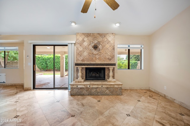 unfurnished living room with a tiled fireplace, ceiling fan, and a healthy amount of sunlight