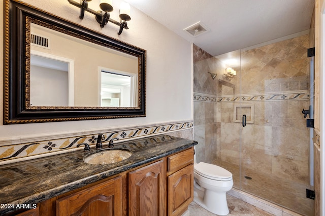 bathroom featuring tile patterned floors, toilet, a shower with shower door, vanity, and tile walls