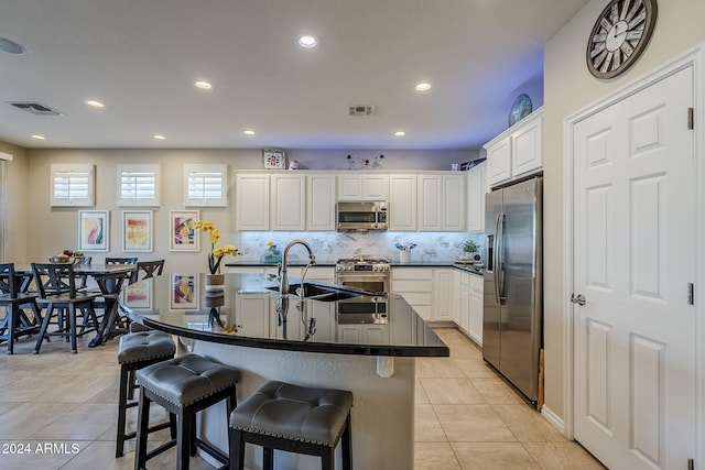 kitchen with white cabinetry, stainless steel appliances, a kitchen island with sink, and decorative backsplash