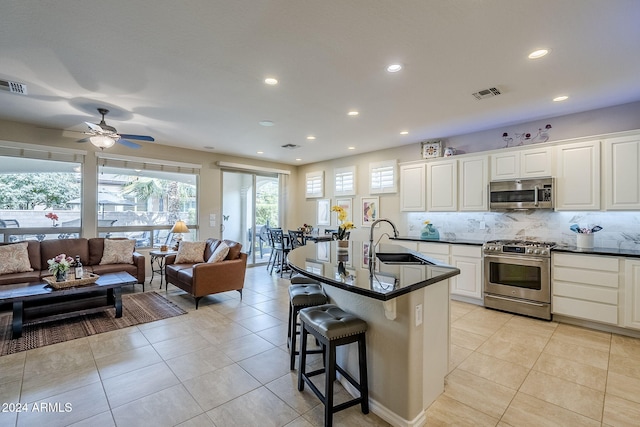 kitchen with sink, appliances with stainless steel finishes, a kitchen island with sink, a kitchen breakfast bar, and white cabinets