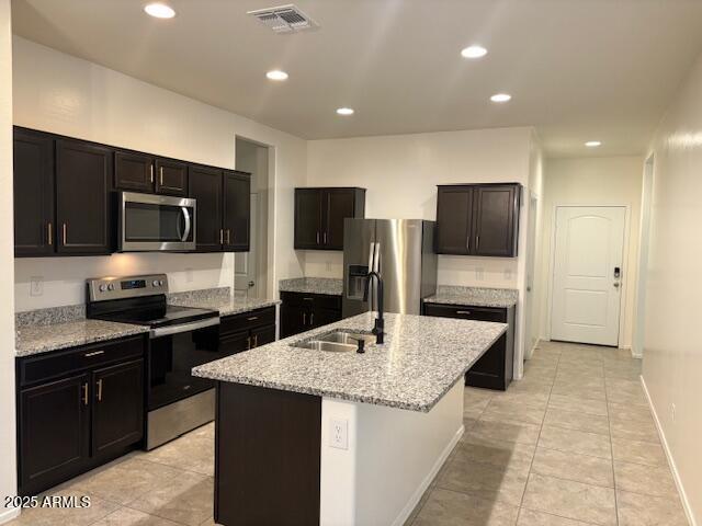 kitchen with a center island with sink, visible vents, appliances with stainless steel finishes, a sink, and light stone countertops