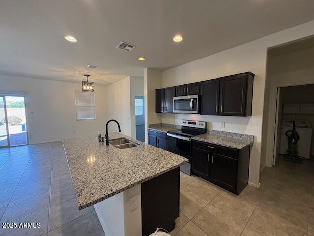 kitchen featuring visible vents, dark cabinets, light stone countertops, stainless steel appliances, and a sink