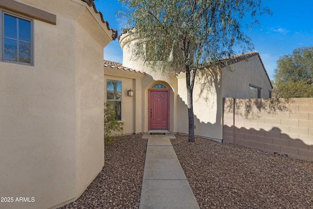 doorway to property featuring stucco siding, a tile roof, and fence
