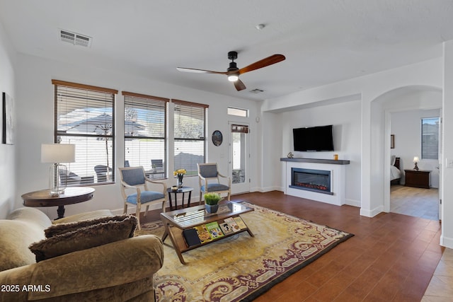 living area with visible vents, wood finished floors, ceiling fan, and a glass covered fireplace
