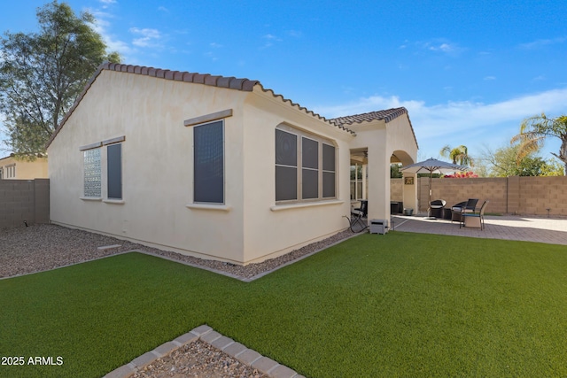 rear view of house featuring a yard, a patio, stucco siding, and a fenced backyard
