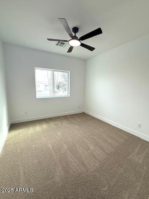 spare room with visible vents, a ceiling fan, baseboards, and dark colored carpet