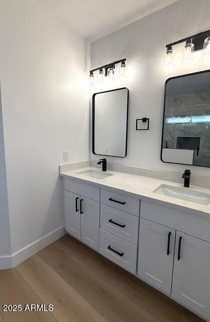 bathroom with a sink, a shower with door, wood finished floors, and double vanity