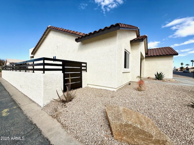 view of property exterior featuring stucco siding, a tile roof, and fence