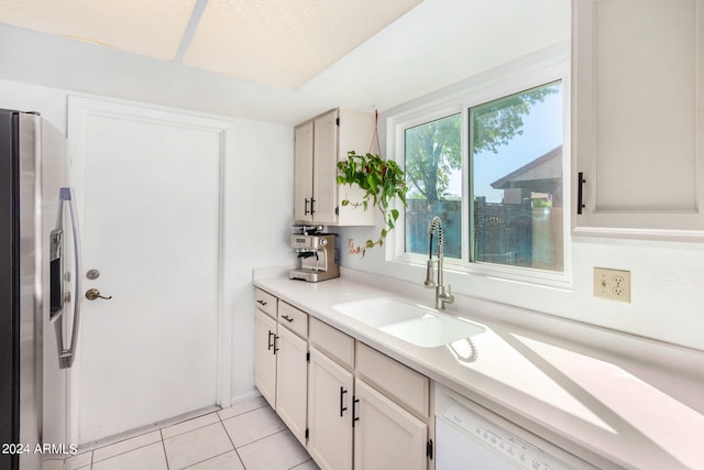 kitchen with sink, stainless steel fridge, white cabinetry, and light tile patterned floors