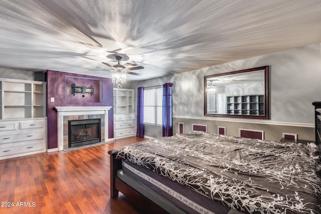 bedroom featuring hardwood / wood-style floors, ceiling fan, a textured ceiling, and a tiled fireplace