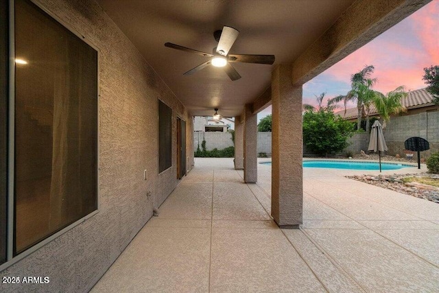 patio terrace at dusk featuring a fenced in pool and ceiling fan