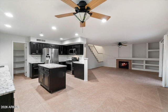 kitchen with stainless steel appliances, light stone countertops, a kitchen island, and ceiling fan