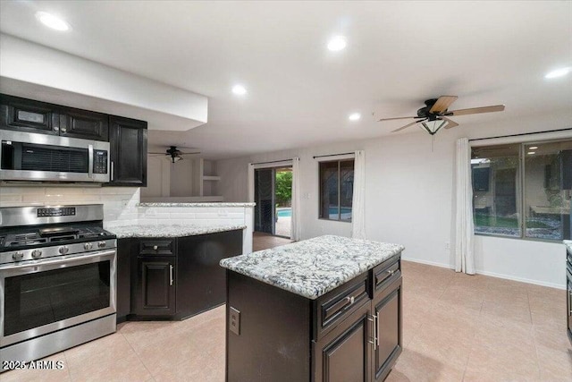 kitchen with ceiling fan, stainless steel appliances, light stone counters, a kitchen island, and decorative backsplash