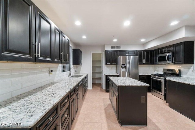 kitchen featuring sink, light stone counters, a center island, light tile patterned floors, and appliances with stainless steel finishes