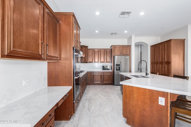 kitchen featuring a breakfast bar, a center island with sink, sink, light stone counters, and stainless steel appliances