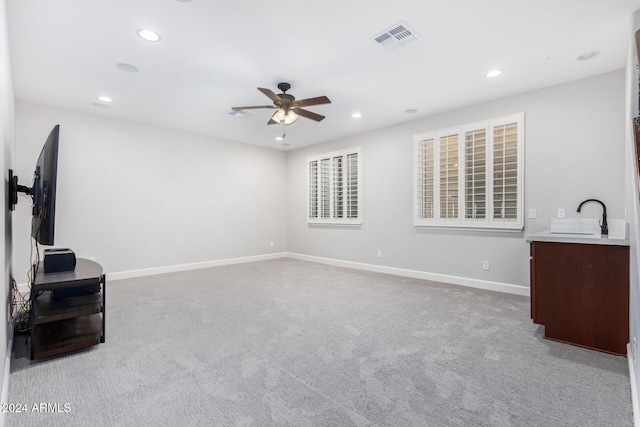 unfurnished living room featuring ceiling fan, sink, and light carpet