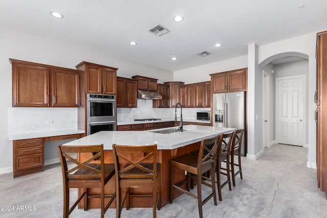 kitchen featuring backsplash, a kitchen island with sink, a kitchen breakfast bar, sink, and appliances with stainless steel finishes