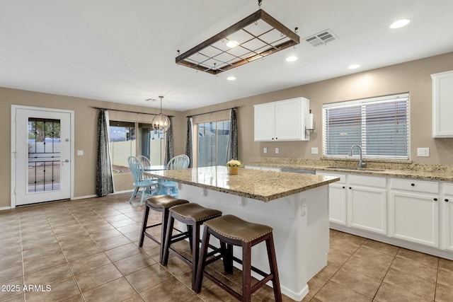 kitchen with white cabinetry, a center island, visible vents, and a sink