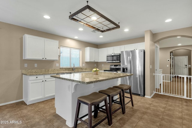 kitchen featuring a kitchen island, light stone countertops, appliances with stainless steel finishes, arched walkways, and white cabinets