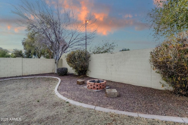 yard at dusk with a fenced backyard and an outdoor fire pit