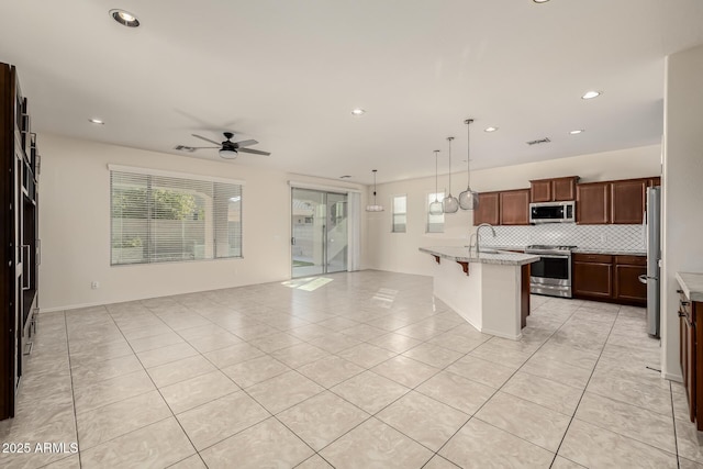 kitchen with appliances with stainless steel finishes, a kitchen bar, an island with sink, decorative backsplash, and hanging light fixtures